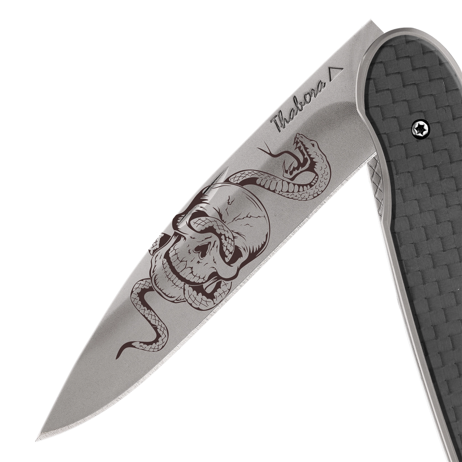 Couteau acier finition titane gris plaquette pleine carbone motif «tête de mort serpent»