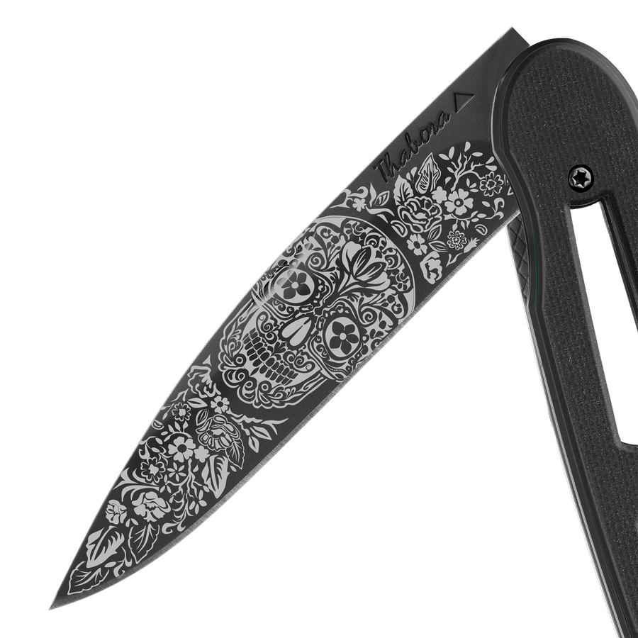 Couteau acier finition titane noir plaquette ajourée résine g10 noir motif «tête mexicaine»